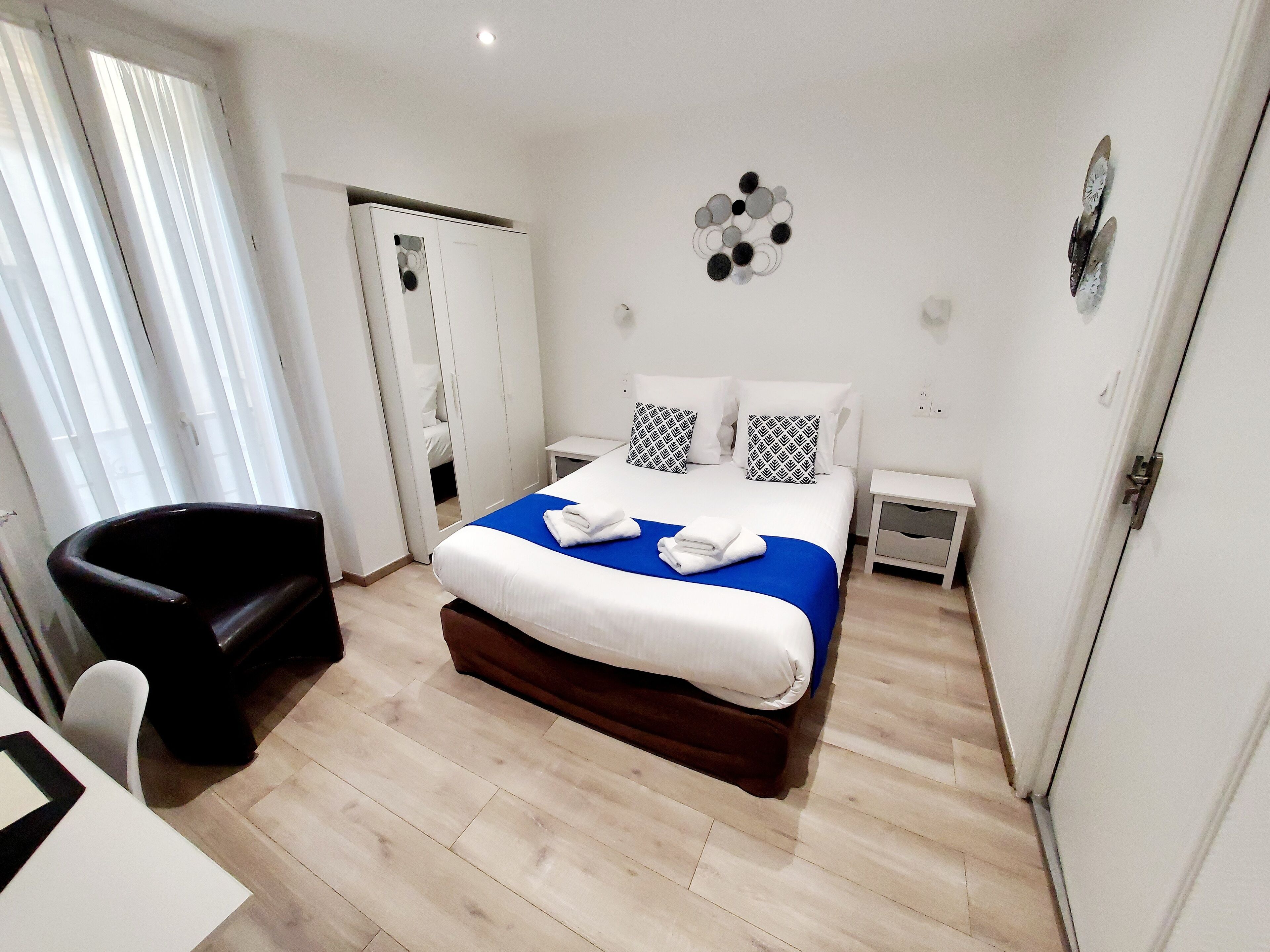 A hotel room with a bed, a chair, a bedside table, and a wardrobe.