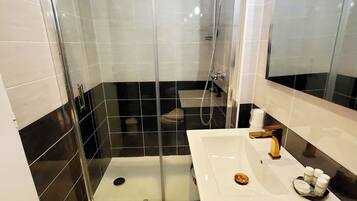 A modern bathroom with a glass-enclosed shower, a white sink with gold fixtures, and black and white tiled walls.