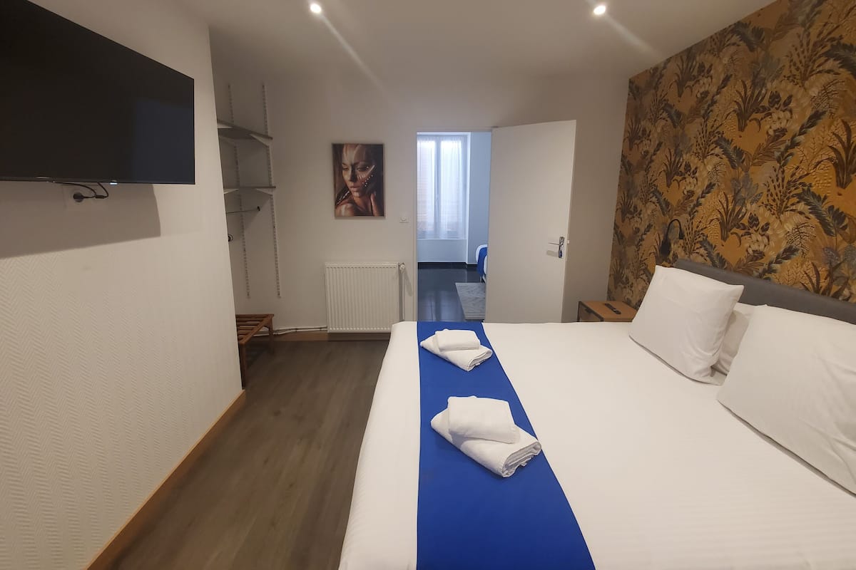 A hotel room with a bed, a flat-screen TV, a radiator, and a door leading to another room.