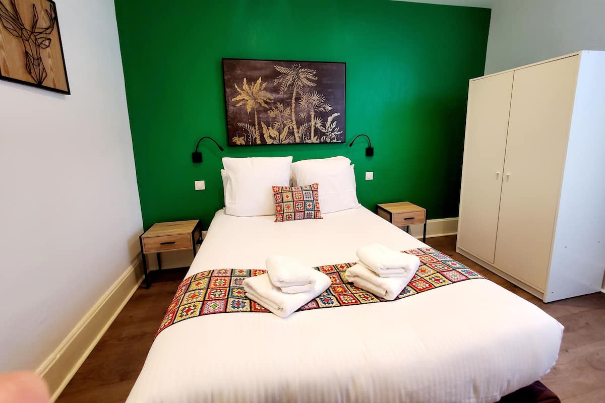 A neatly made bed with white linens, a colorful quilt, and two towels folded at the foot of the bed.