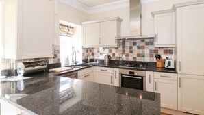 A modern kitchen with white cabinets, a granite countertop, a gas stove, and a coffee maker. - Silver How (Ambleside)