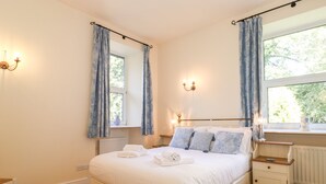 A bedroom with a bed, bedside tables, a nightstand, a window with curtains, and a radiator. - Silver How (Ambleside)
