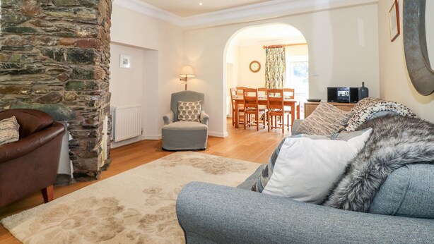 A cozy living room with a stone wall, a brown leather sofa, a grey armchair, and a patterned rug. - Silver How (Ambleside)