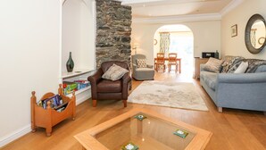 A living room with a stone wall, a brown leather armchair, a blue sofa, a wooden coffee table, and a dining area with a table and chairs. - Silver How (Ambleside)