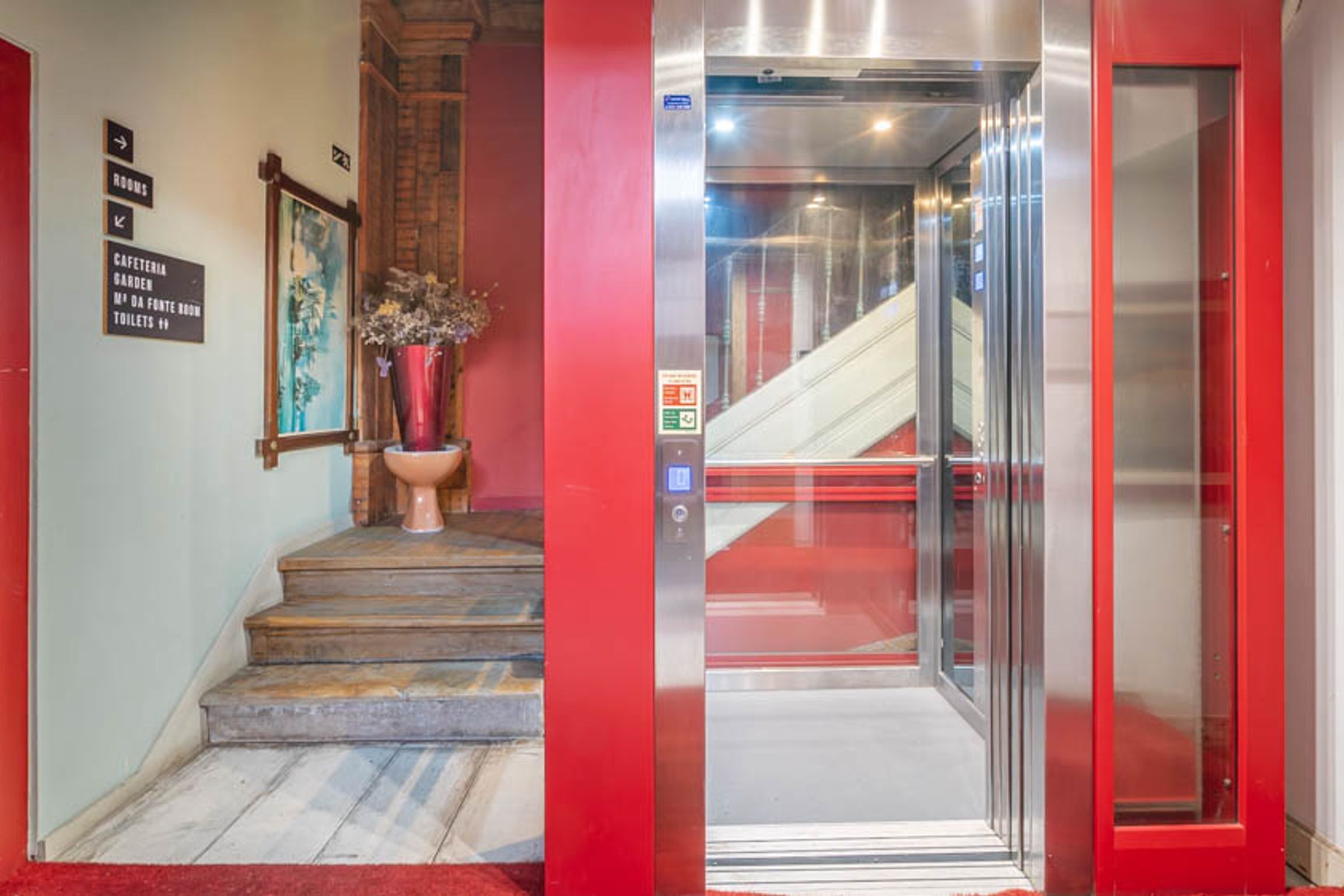 Ein Aufzug mit roter Außenwand und Glastür, der zu einer Treppe führt.