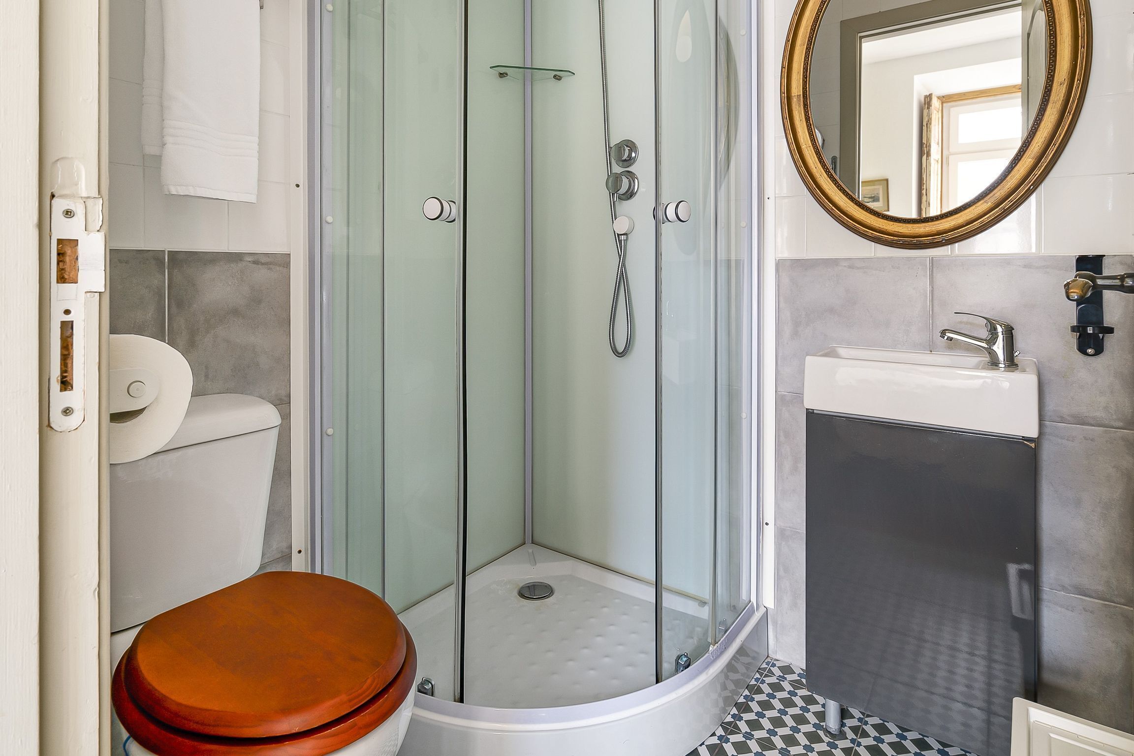 A bathroom with a glass-enclosed shower, a white sink, and a wooden toilet seat.