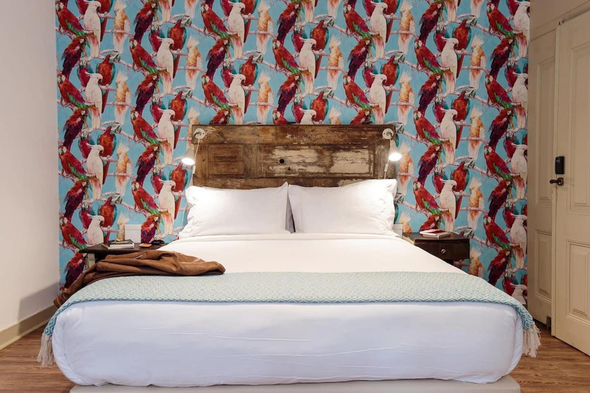 A bed with white linens, a wooden headboard, and a patterned wall behind it.