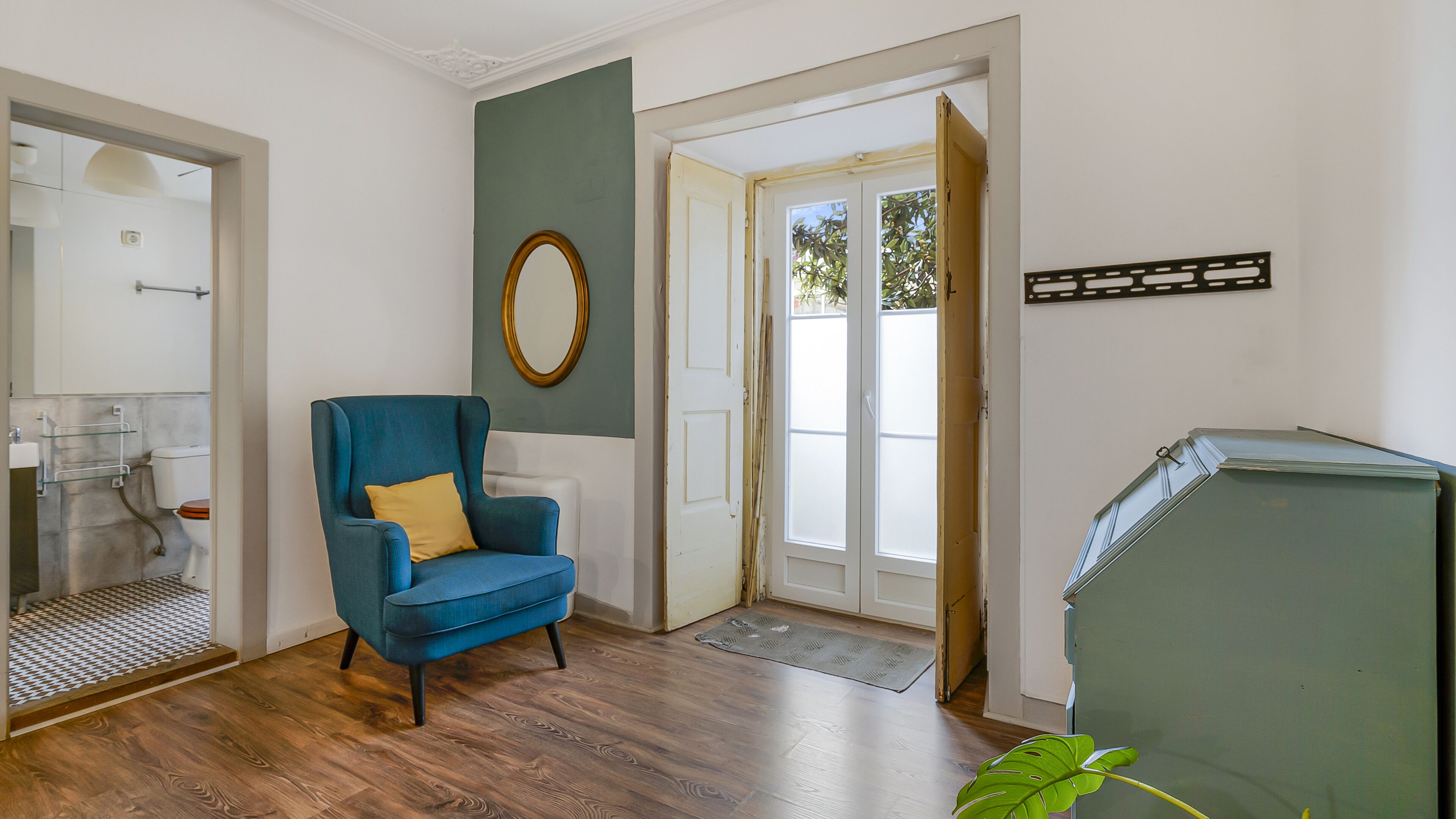 A room with a blue armchair, a mirror, a door leading outside, and a green cabinet.