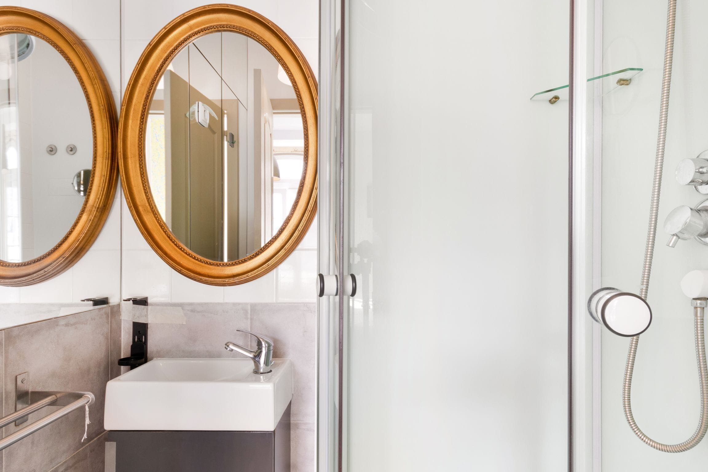 A modern bathroom with two gold-framed mirrors, a white sink, and a glass-enclosed shower.