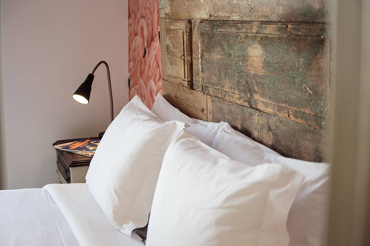 A bed with white linens, a lamp on a bedside table, and a wooden headboard.