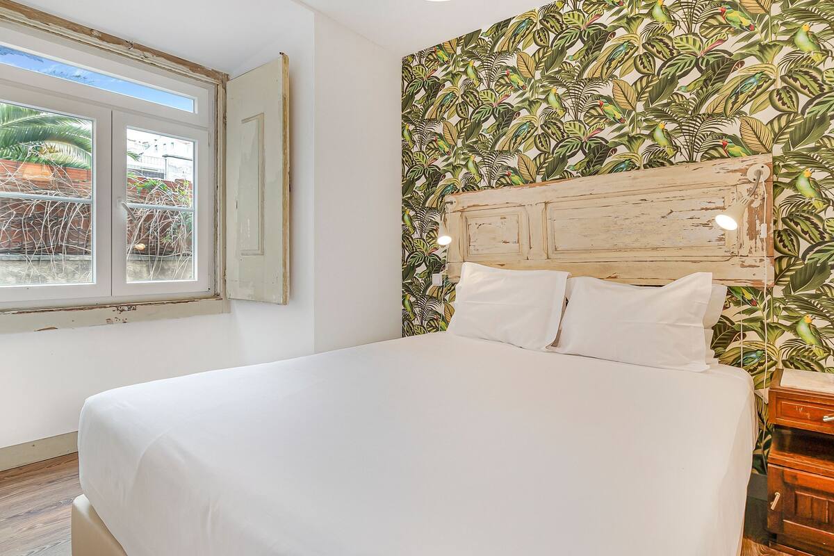 A bedroom with a bed, a window, and a wall with a tropical leaf pattern.