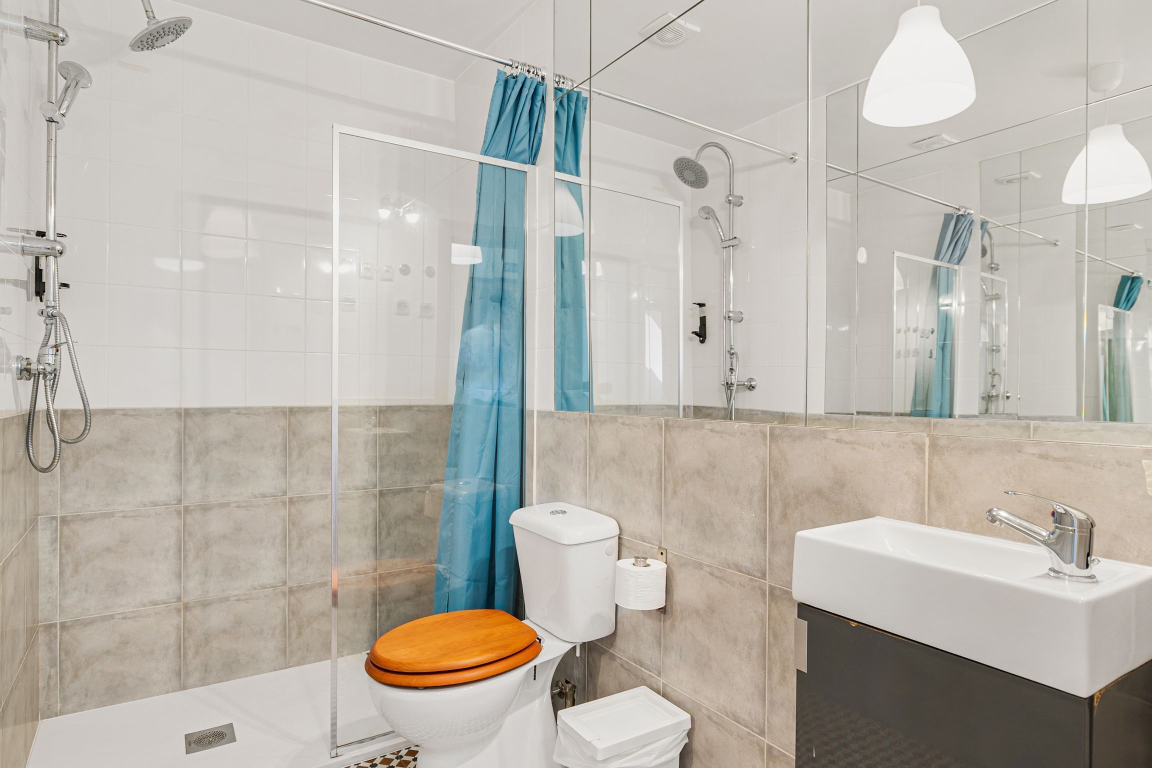 Ein modernes Badezimmer mit Duschkabine aus Glas, einem weißen Waschbecken mit Spiegel und einem hölzernen Toilettendeckel.