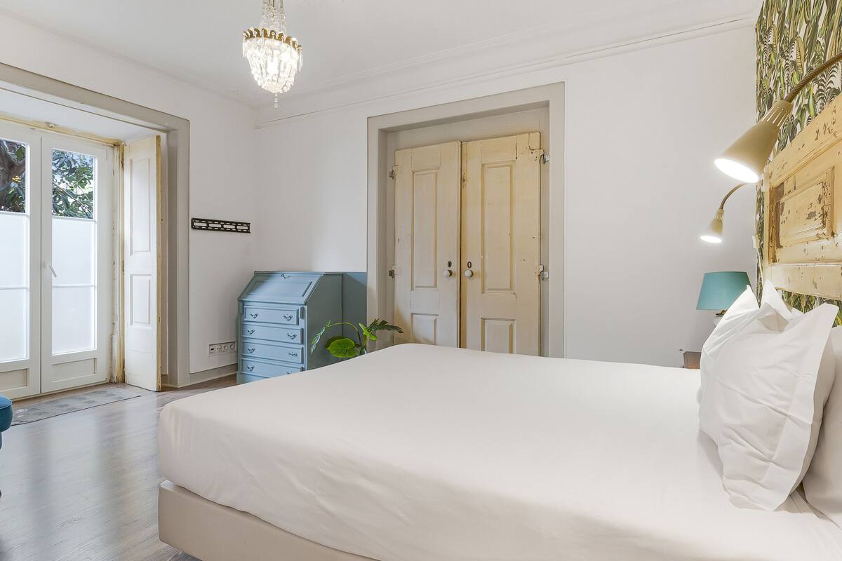 A bedroom with a large bed, a dresser, a chandelier, and a view through a door.