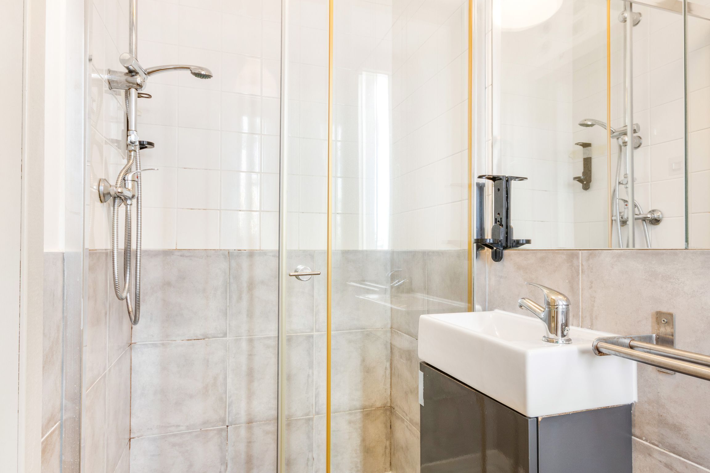 Een moderne badkamer met een douchecabine van glas, een witte wastafel met een chromen kraan en een spiegel boven de wastafel.