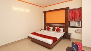 A hotel room with a bed, a ceiling fan, a wall-mounted air conditioner, and a red curtain.