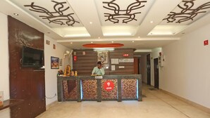 A hotel reception area with a reception desk, a television mounted on the wall, and a ceiling with decorative patterns.