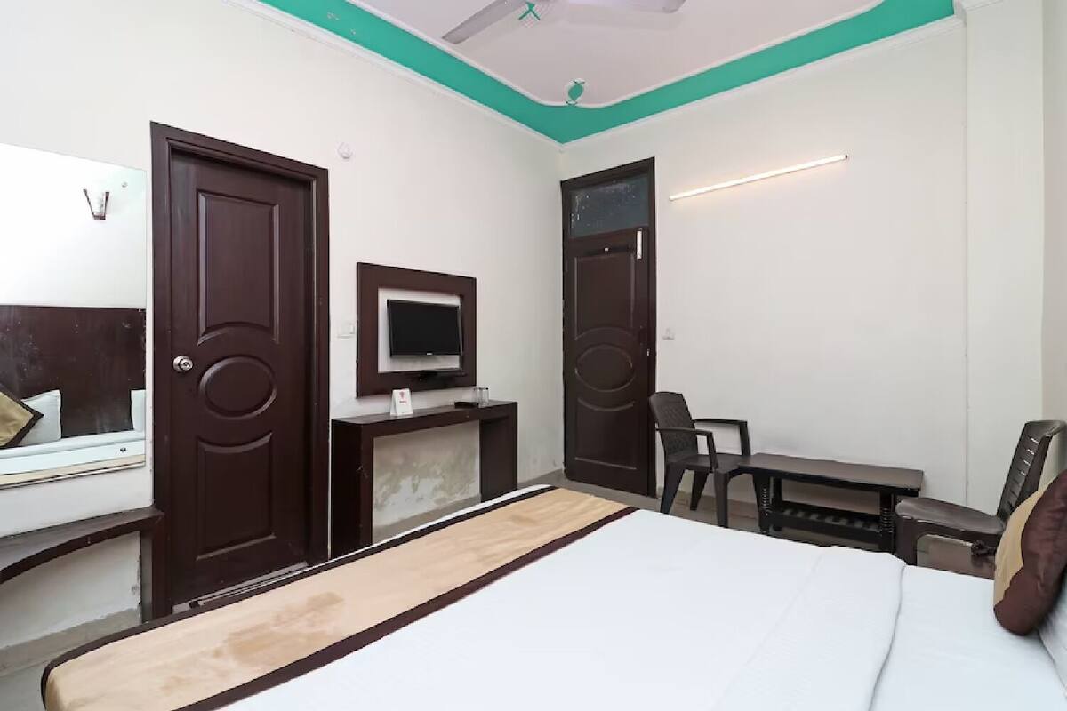 Quarto de hotel com uma cama, uma mesa, uma cadeira, uma televisão e duas portas.