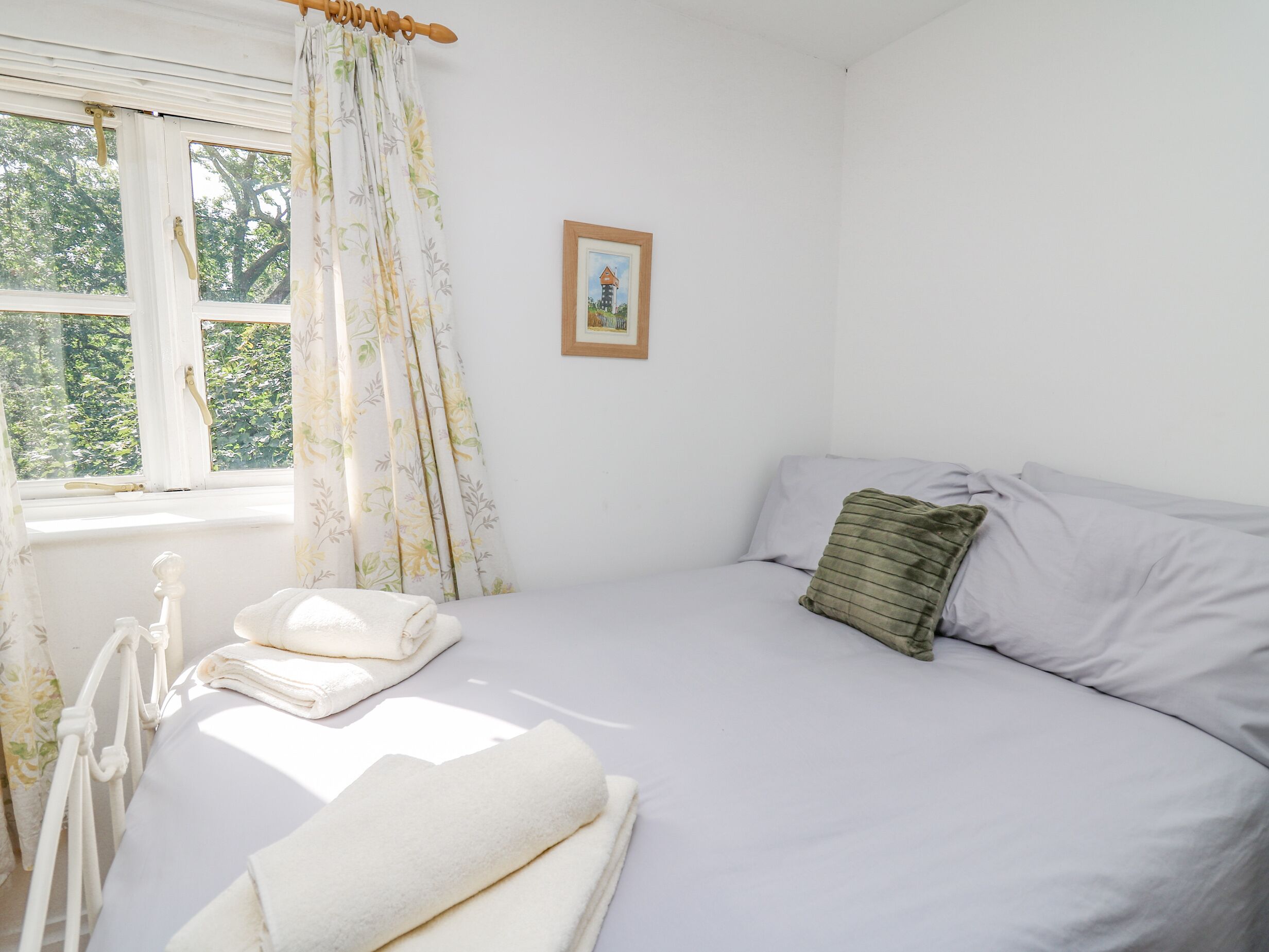 A bedroom with a bed, a window with curtains, a radiator, and a framed picture on the wall.