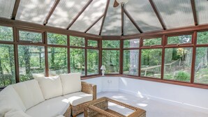 A conservatory with a large sectional sofa and wicker furniture, large windows offering a view of the outdoors. - The Coach House at Plas Dolguog (Machynlleth)