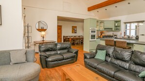 A spacious living area with leather sofas, a wooden coffee table, and a dining area with a chandelier. - The Coach House at Plas Dolguog (Machynlleth)
