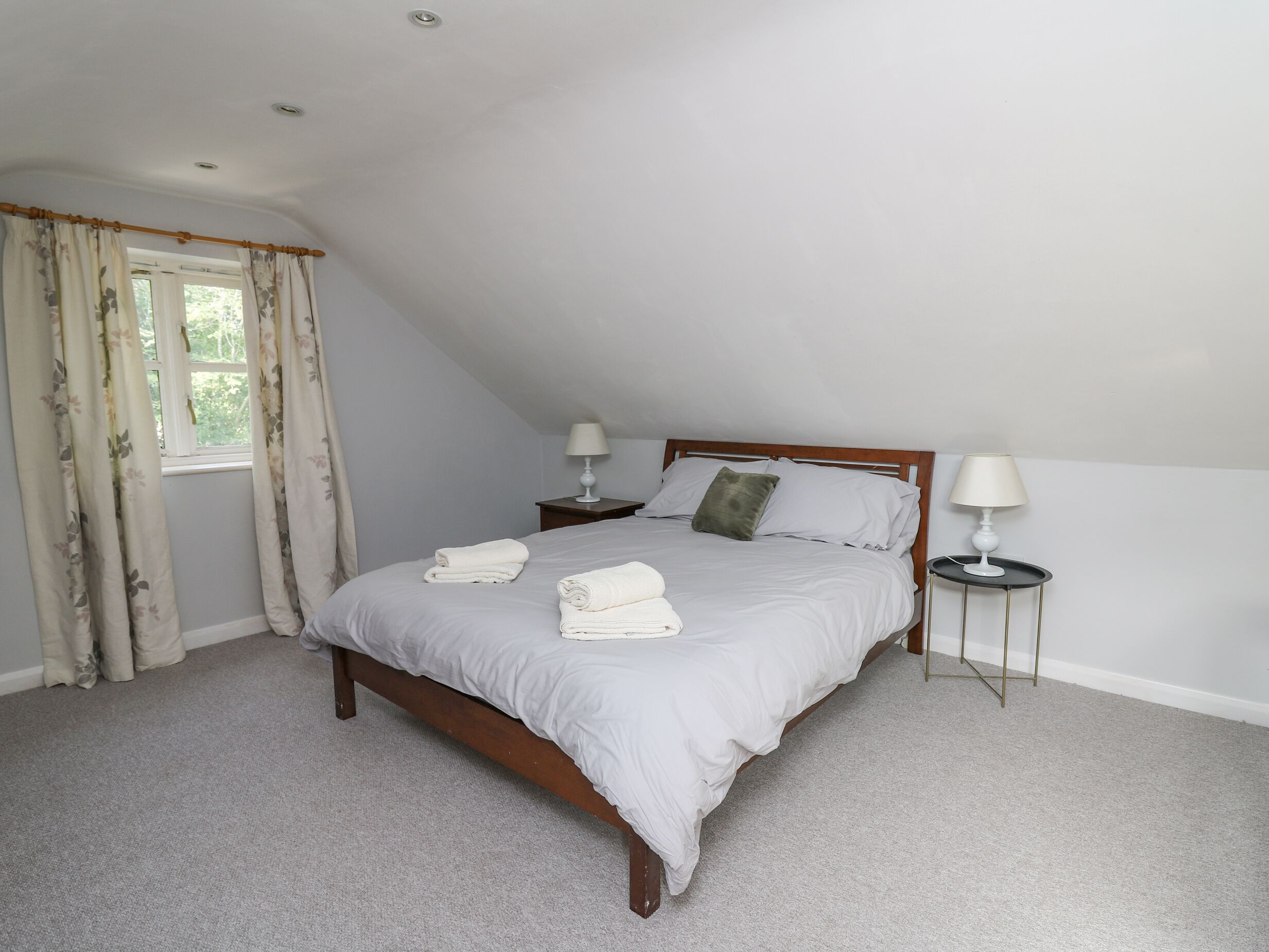 A bedroom with a single bed, two bedside tables with lamps, a window with curtains, and a carpeted floor.