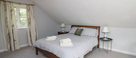 A bedroom with a single bed, two bedside tables with lamps, a window with curtains, and a carpeted floor.