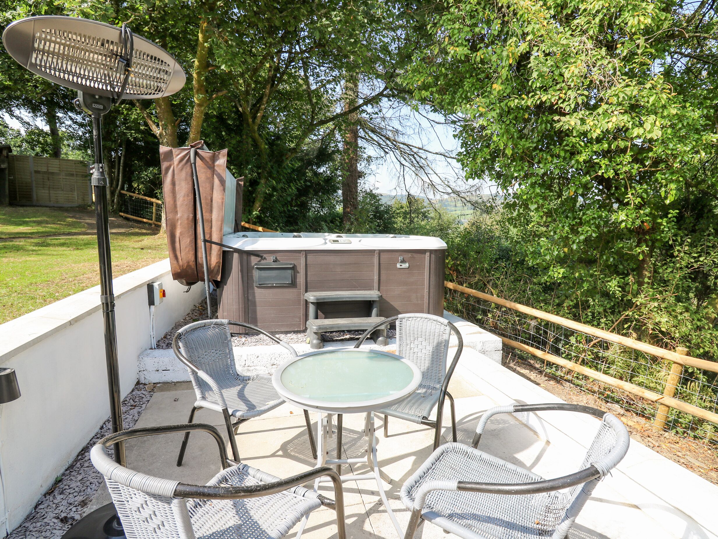 An outdoor patio with a hot tub, wicker chairs, and a table.