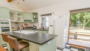 A kitchen with a central island, bar stools, a refrigerator, and a view of the outdoors. - The Coach House at Plas Dolguog (Machynlleth)