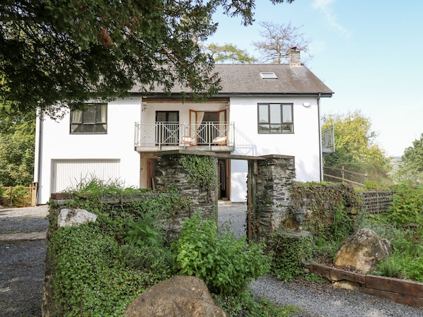 A two-story house with a balcony, stone walls, and a gravel driveway. - The Coach House at Plas Dolguog (Machynlleth)