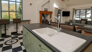 A kitchen with a large window, a sink, and a dining area with bar stools. - The Coach House at Plas Dolguog (Machynlleth)