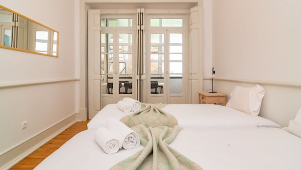 A hotel room with a large bed, a mirror, a small table, and a view through the door.