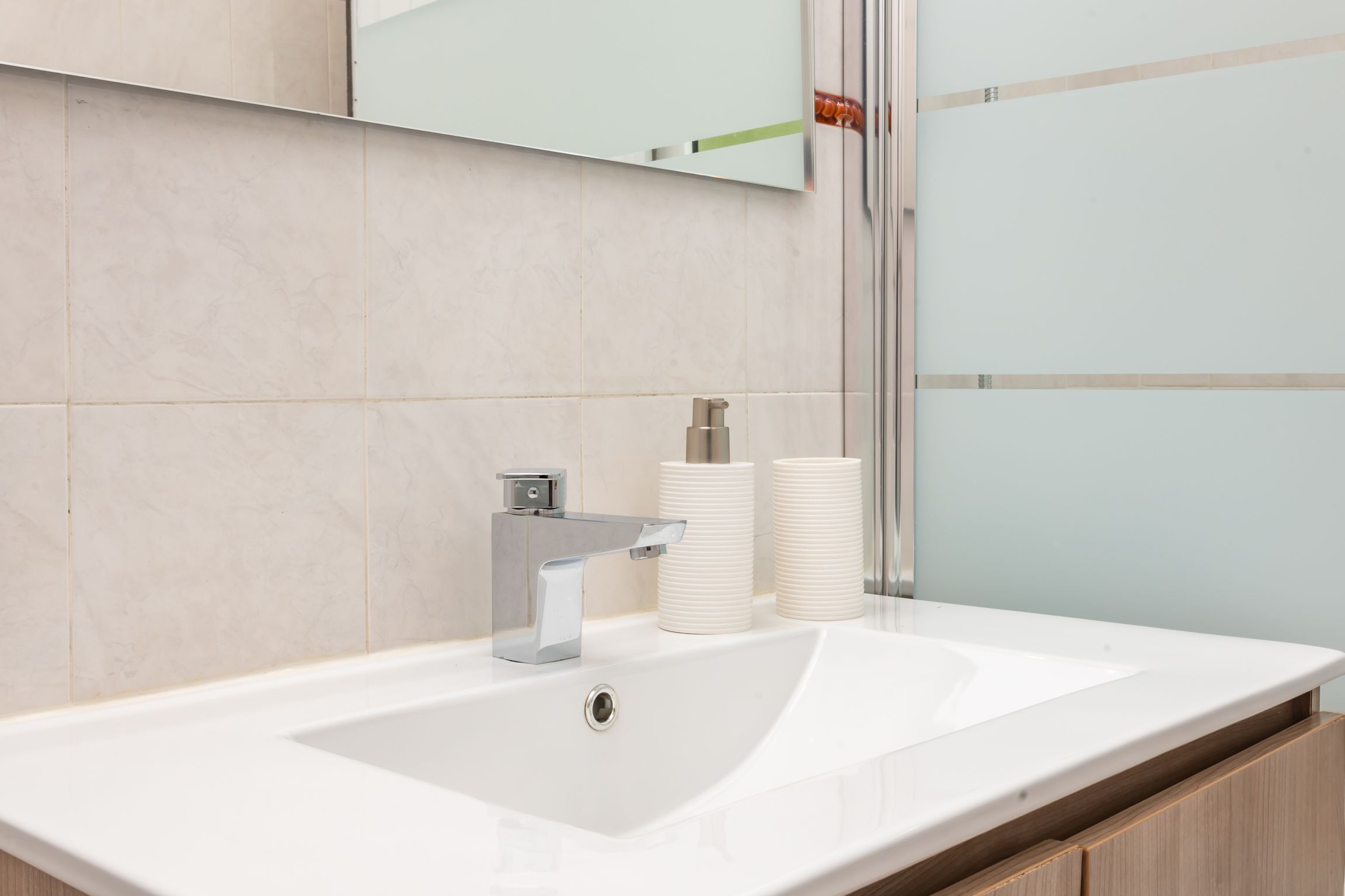 A modern bathroom with a white sink, chrome faucet, and two white cylindrical containers on the counter.