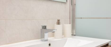 A modern bathroom with a white sink, chrome faucet, and two white cylindrical containers on the counter.