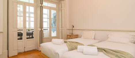 A bedroom with two beds, a wooden floor, a green rug, and a view through a door.