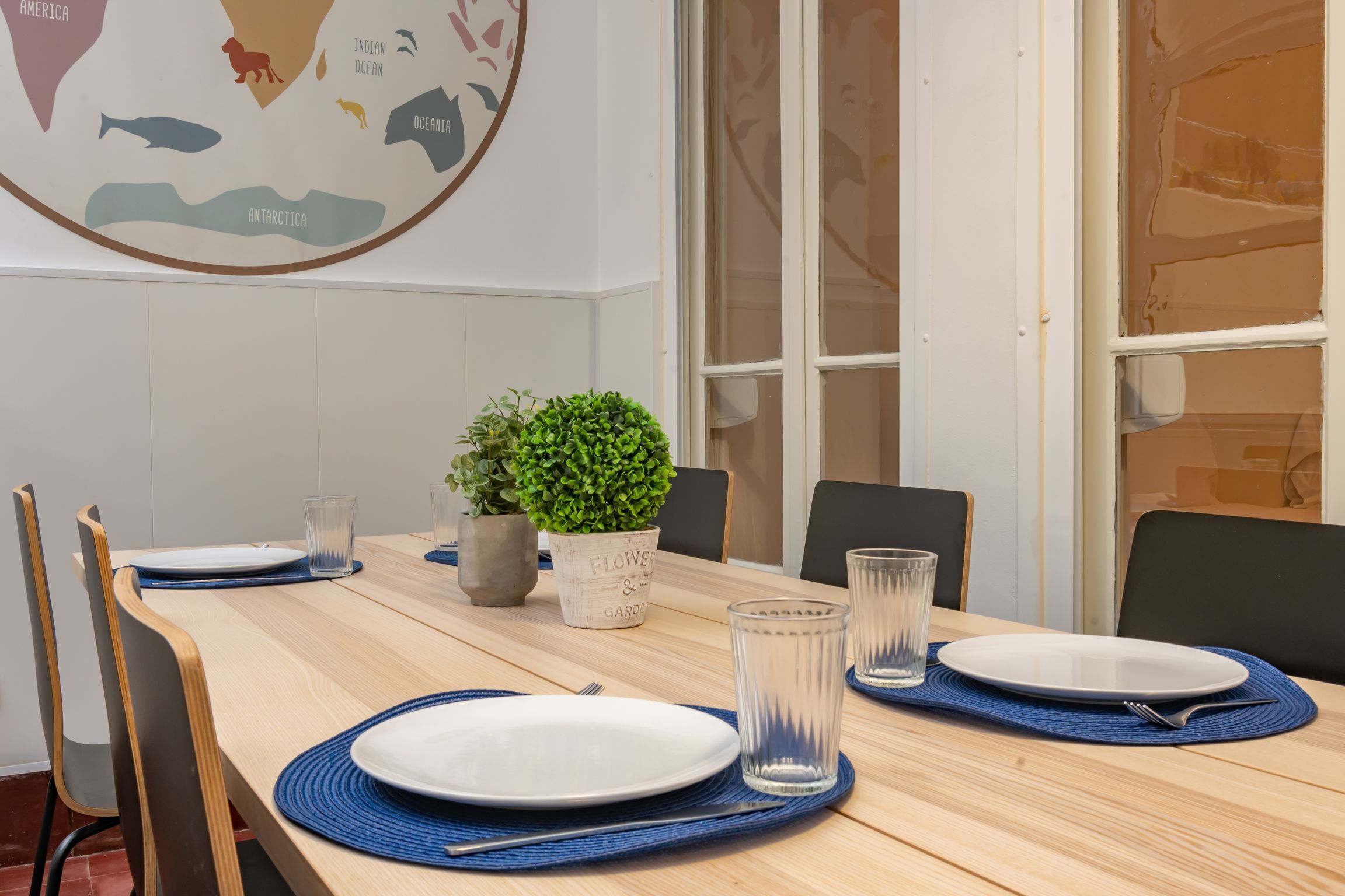 Een eettafel gedekt met borden, glazen en een plant in een kamer met een kaart aan de muur.