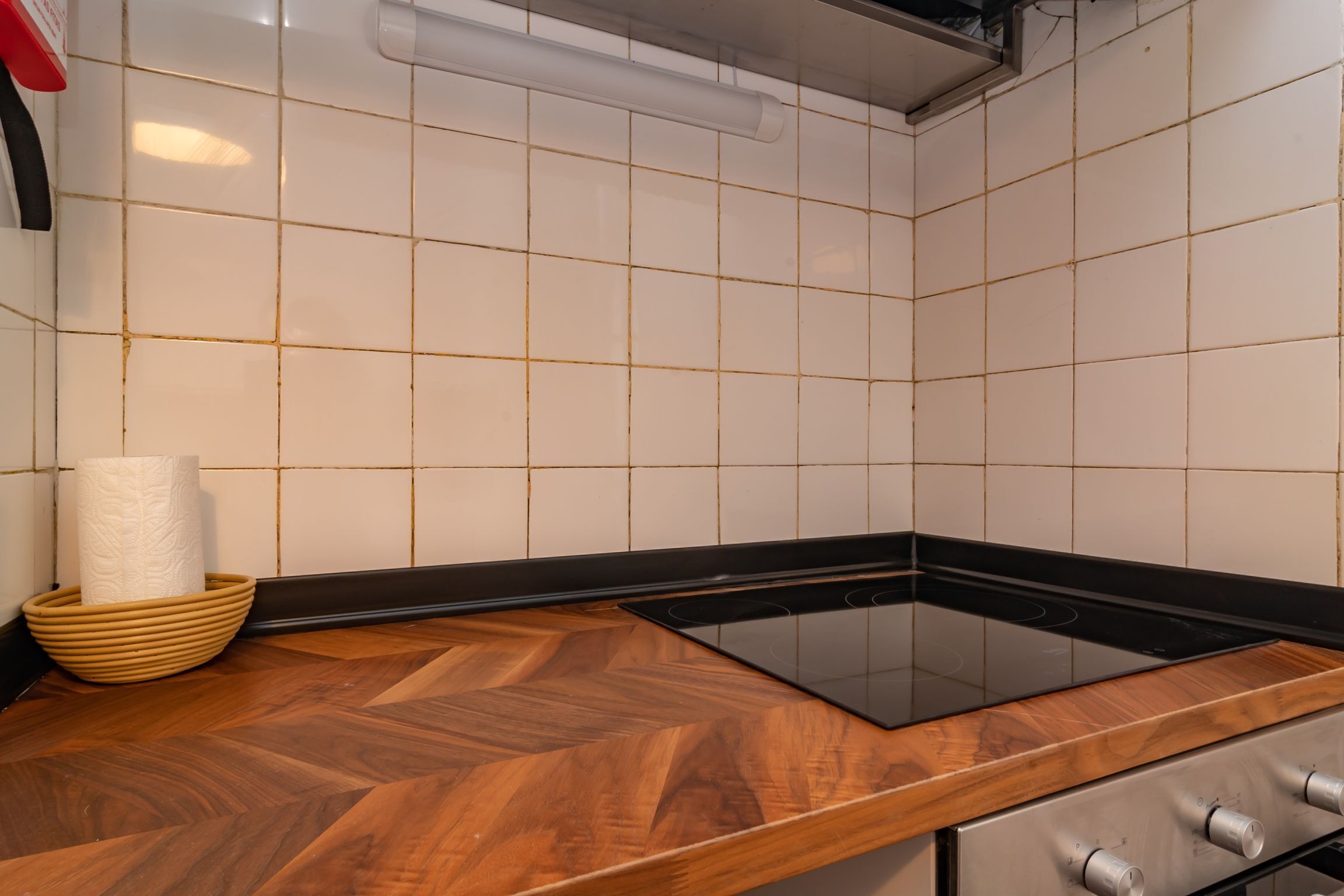 Een keuken met witte betegelde wanden, een houten aanrechtblad en een zwart inductiekookveld.