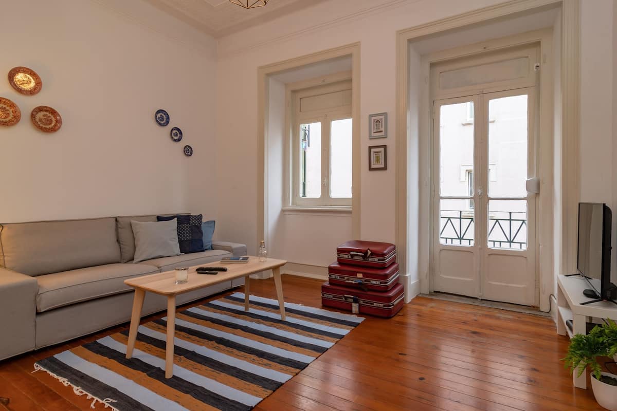 A living room with a sofa, a coffee table, a striped rug, a stack of suitcases, and a TV stand.