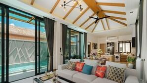 A spacious living room with a large sofa, a coffee table, and a view of a swimming pool. - Rawayana Villas (Rawai)