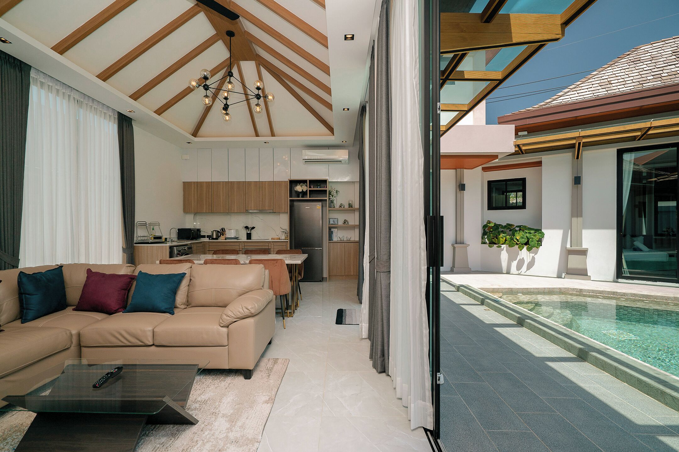 A modern living room with a sofa, coffee table, and a view of the kitchen and pool.