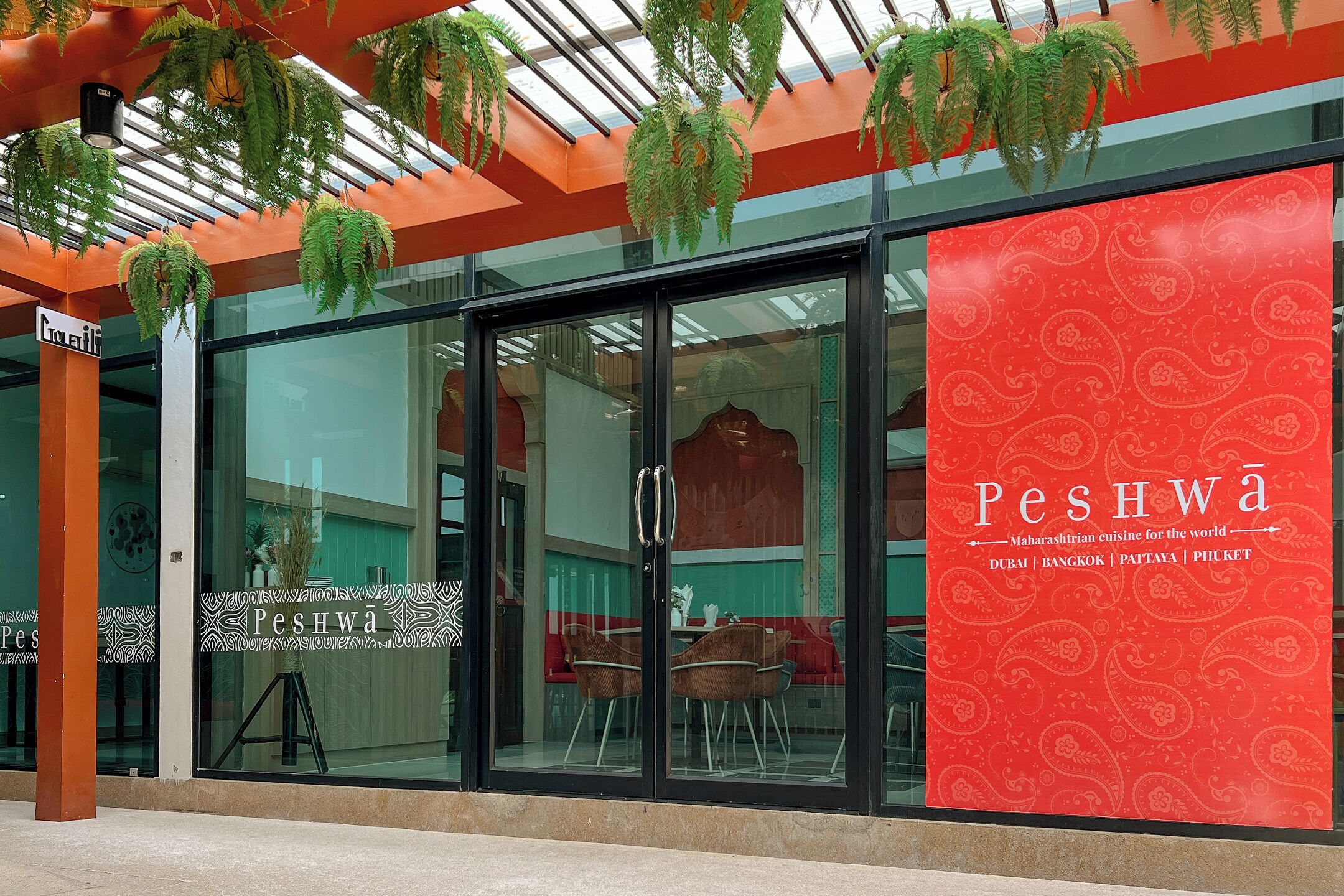 Un restaurante con fachada de vidrio, pared con diseño rojo y plantas colgantes.