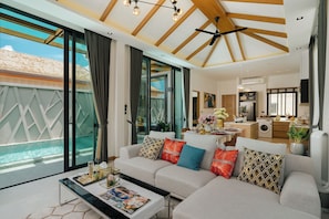 A modern living room with a sofa, coffee table, and large windows overlooking a pool. - Rawayana Villas (Rawai)