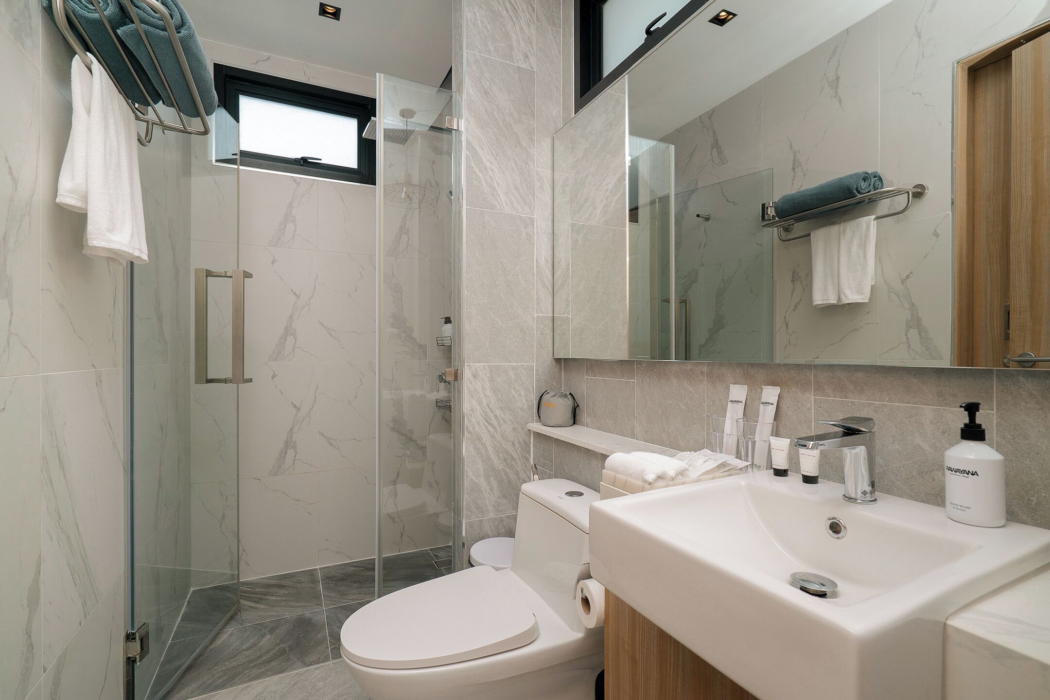 A modern bathroom with a glass shower enclosure, a toilet, a sink with toiletries, and a mirror.