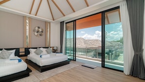A bedroom with two beds, a large sliding glass door, and a view of the cityscape. - Rawayana Villas (Rawai)