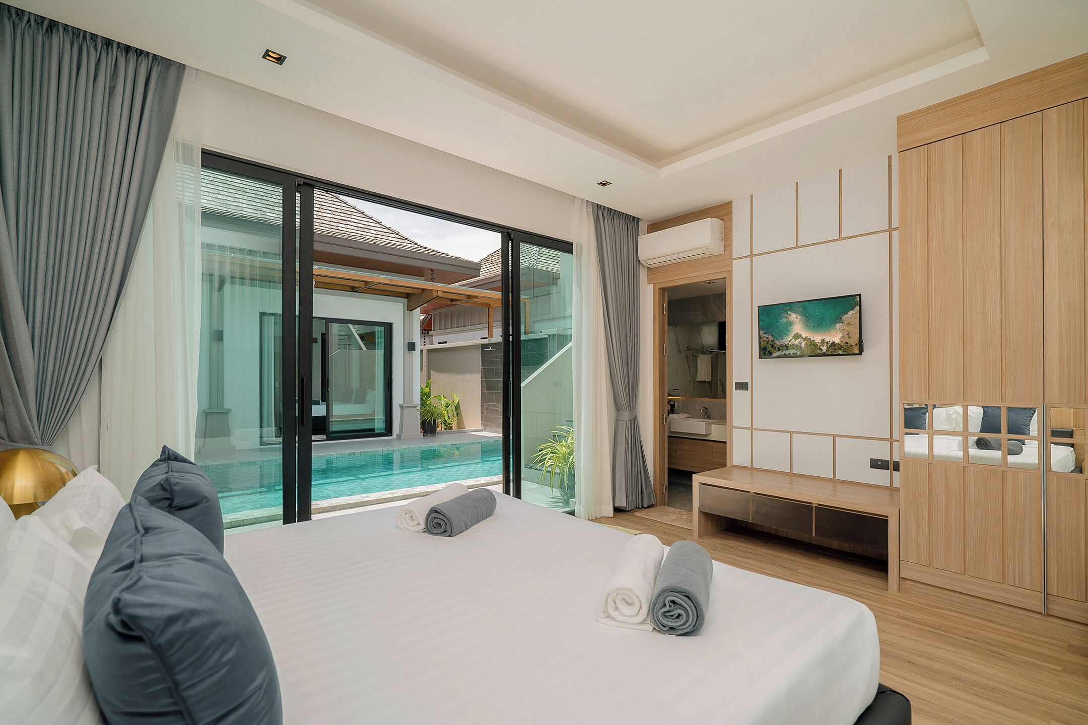 A modern hotel room with a large bed, a view of a swimming pool, and a wooden wardrobe.