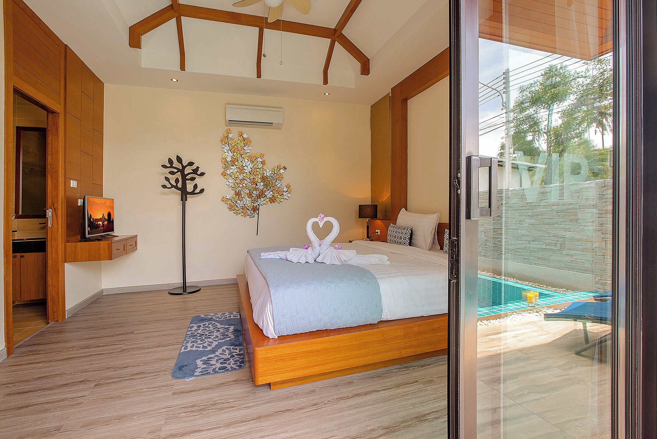 A bedroom with a bed, bedside table, wall art, and a view of the outside.
