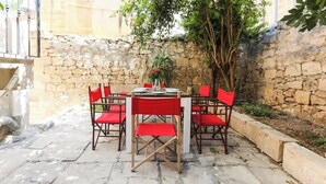 A stone-walled outdoor seating area with a round table and red chairs. - RM4 Chambre en étage - Côté Ville (Sliema)