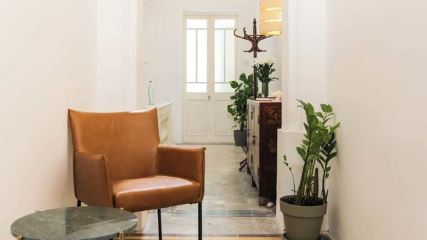 A hallway with a patterned floor, a brown leather chair, a small table, and a potted plant. - RM4 Chambre en étage - Côté Ville (Sliema)