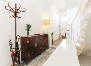A hallway with a coat rack, a wooden cabinet, a lamp, and a staircase.
