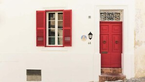 A white building with a red door and window shutters, a small window with a white frame, and a number '44' on the wall. - RM4 Chambre en étage - Côté Ville (Sliema)