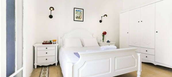 A white bedroom with a bed, nightstands, a wardrobe, and wall-mounted lamps.